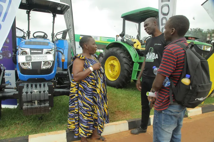 Visitors standing beside tractors at an agricultural exhibition.